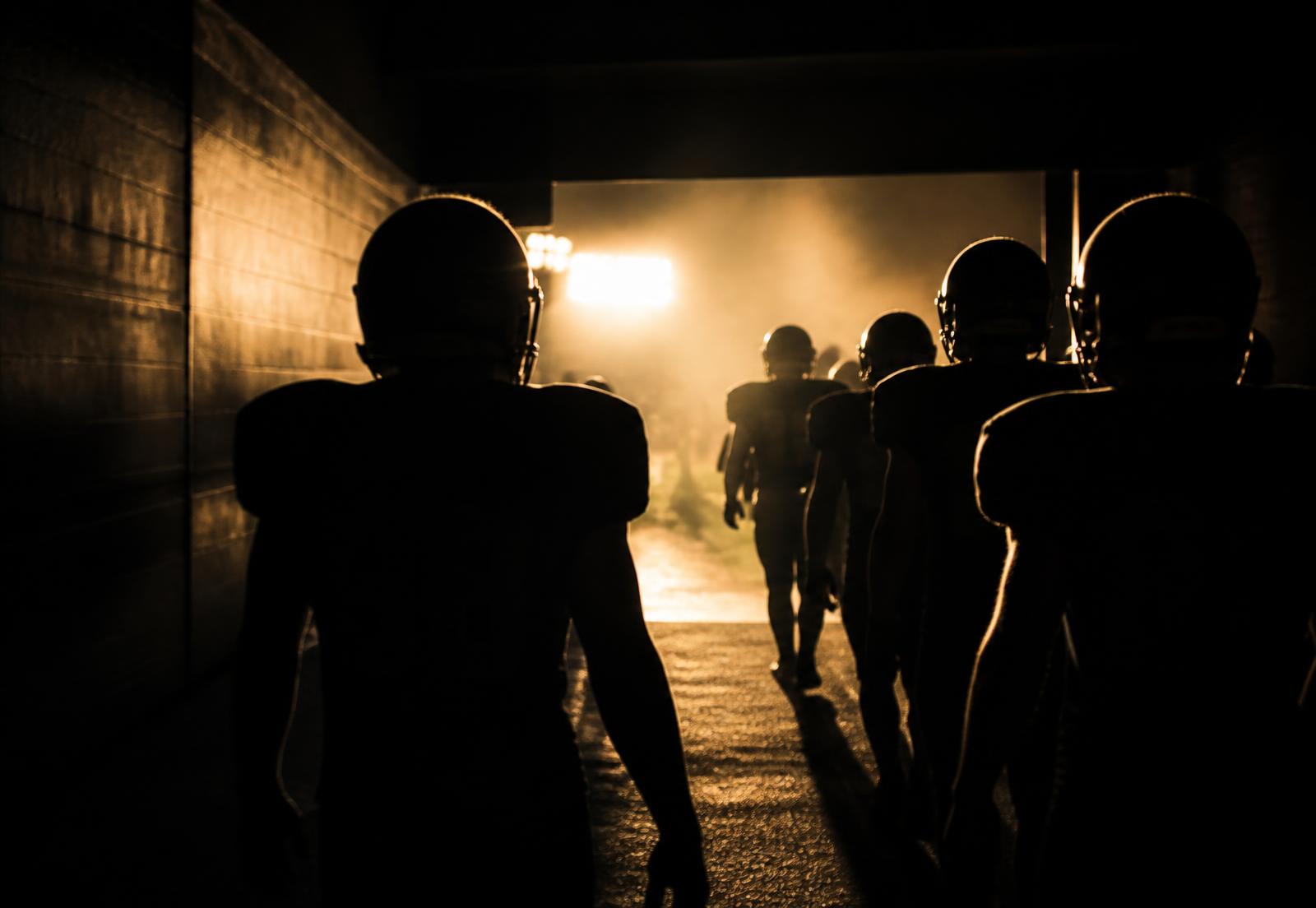 High school football team walking out of the tunnel under stadium lights